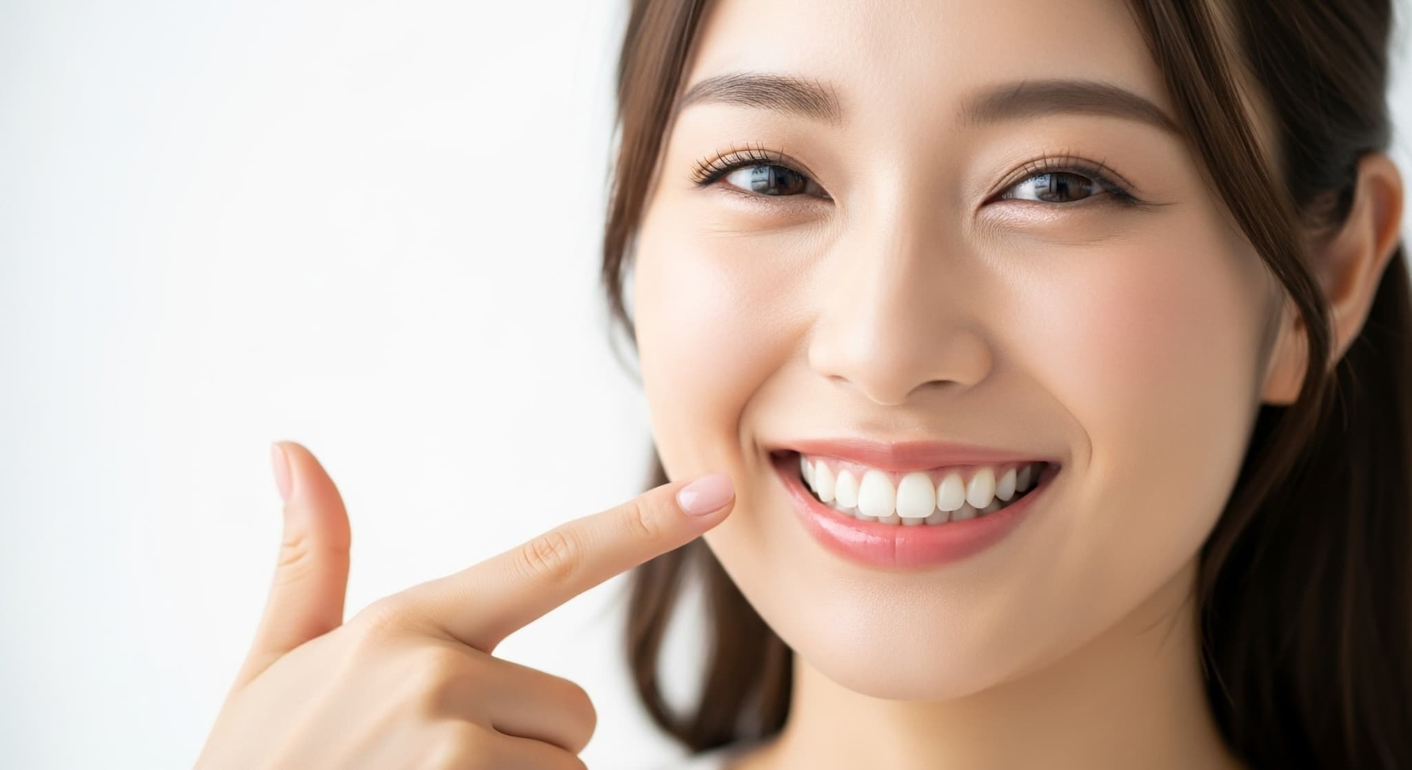 マウスピース矯正で綺麗になった歯を指さす女性