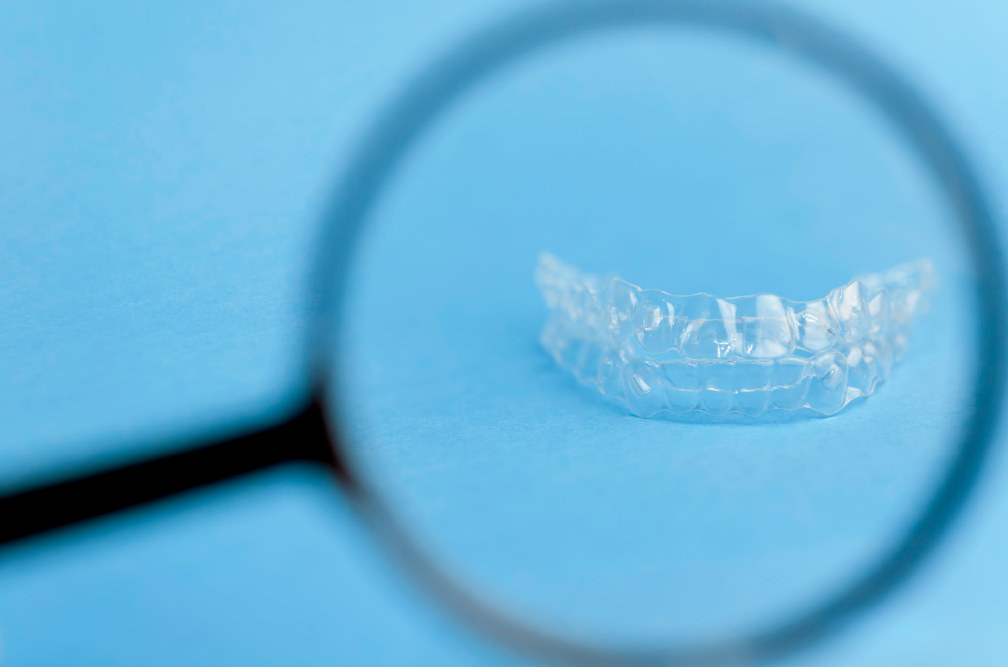 マウスピース矯正の装置が浮く原因は何かマウスピースを虫眼鏡でチェックしているイメージ